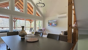 Een eethoek met een grote tafel, stoelen, een vaas en een mand. Er zijn ramen met houten kozijnen en een plafondventilator.
