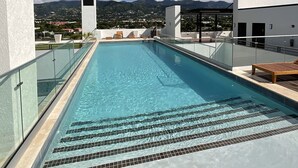 Una piscina en la azotea con agua cristalina, rodeada de arquitectura moderna y vistas a montañas distantes.