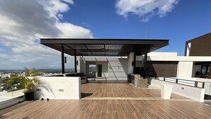 Una terraza en la azotea con suelo de madera, un espacio de estar cubierto y vistas a la ciudad.