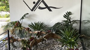 Fachada moderna de un edificio con un logotipo, una fuente de agua y varias plantas.