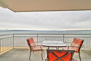 Un balcon avec une table et des chaises, donnant sur une étendue d’eau et sur une terre lointaine.