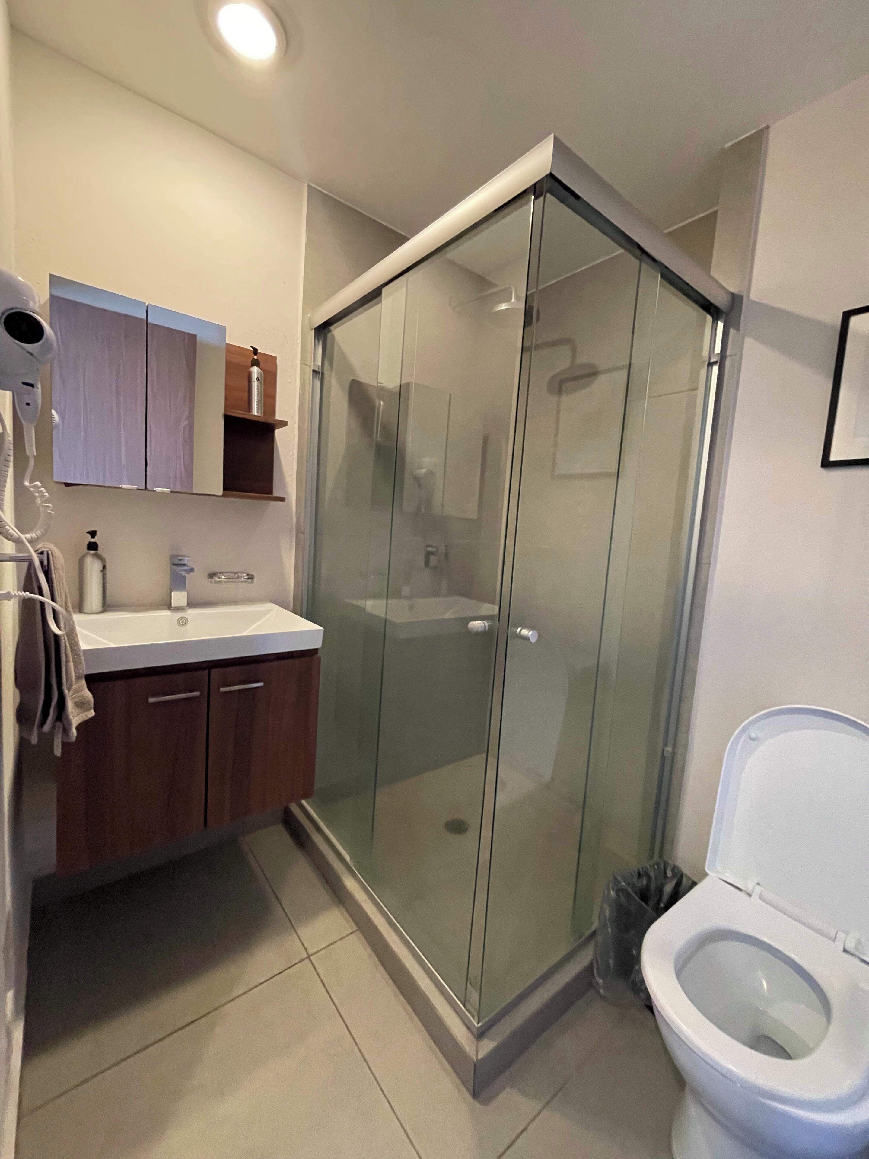 A modern bathroom with a glass shower enclosure, a white toilet, and a vanity with a mirror and cabinets.