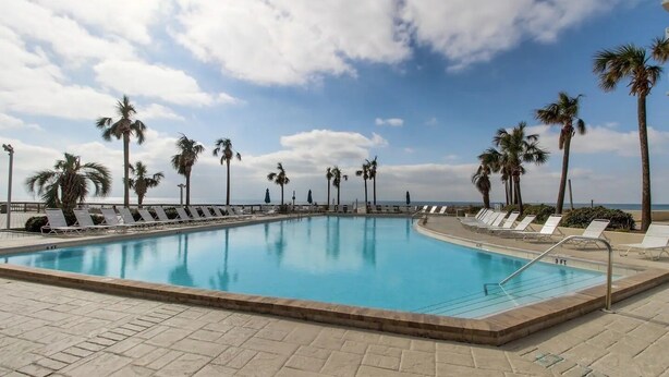 A swimming pool with lounge chairs and palm trees, surrounded by a tiled deck.