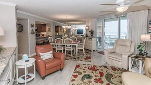 A spacious living room with a dining area, a balcony with a view, and a kitchen in the background.