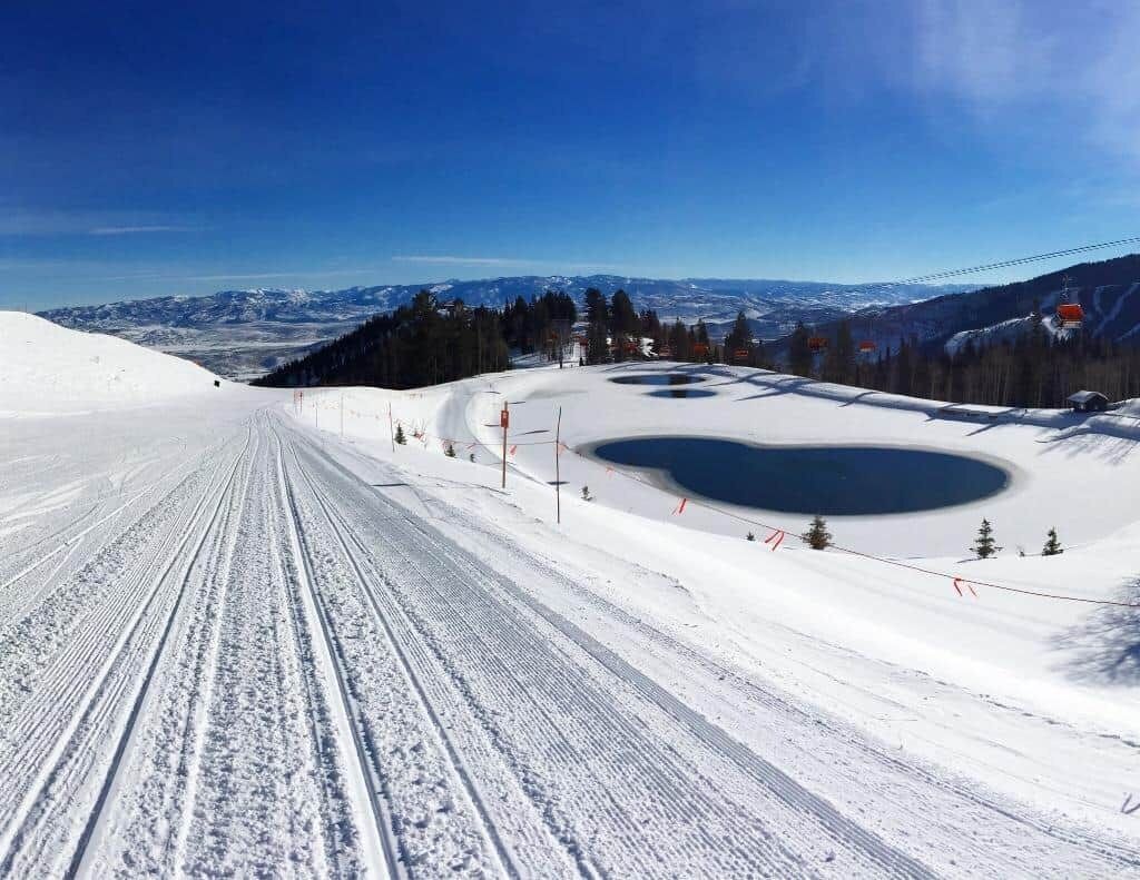 Une piste de ski enneigée, avec un ciel dégagé, un télésiège et un lac.