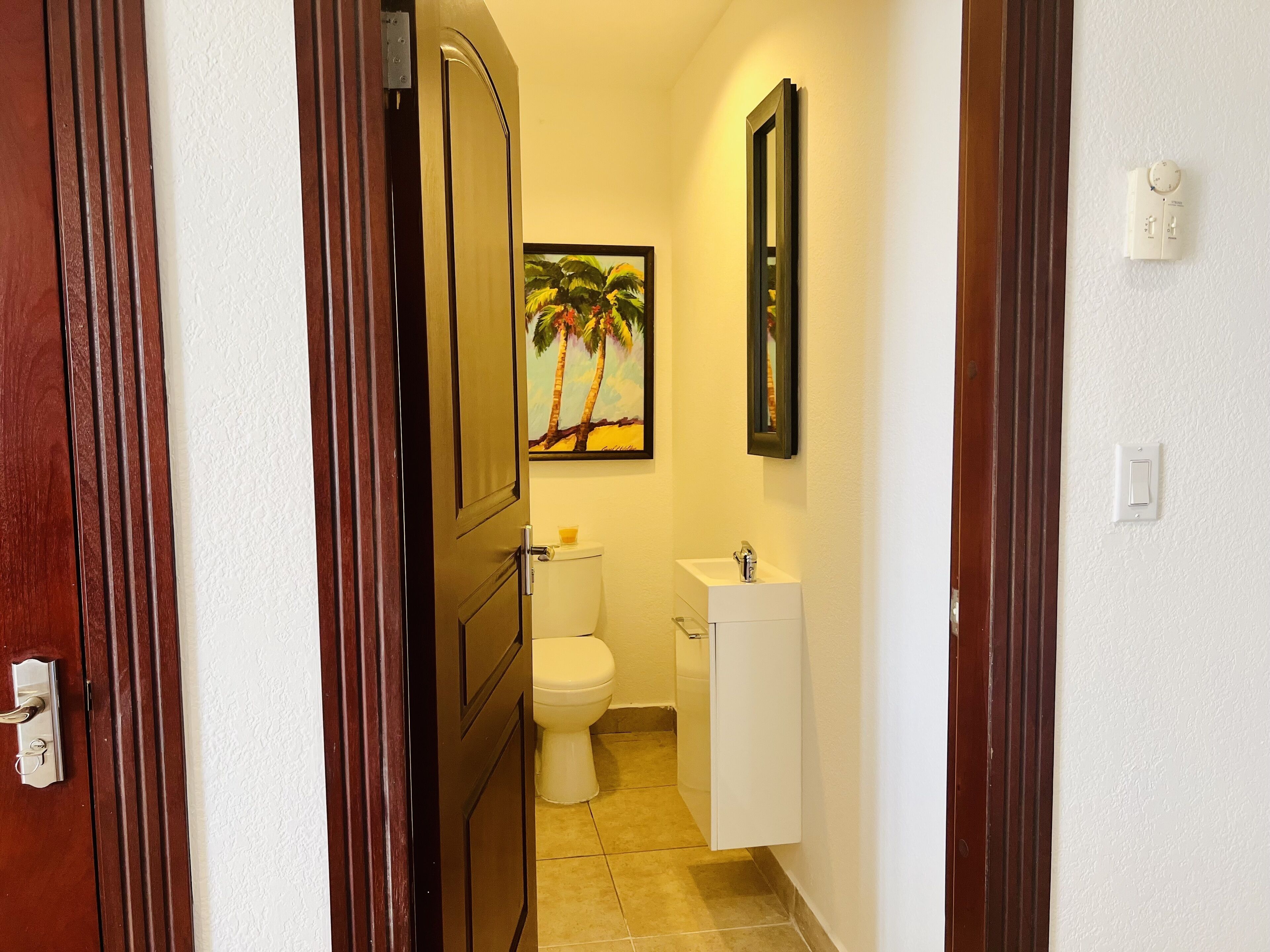 Ein schmaler Flur, der zu einem Badezimmer mit Toilette, Waschbecken und einem Palmenmotiv führt.