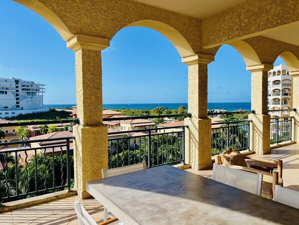 A balcony with a table and chairs, overlooking a coastal area with buildings and a clear blue sky. - Rendezvous in St. Martin - Tropical Waves (Sint Maarten)