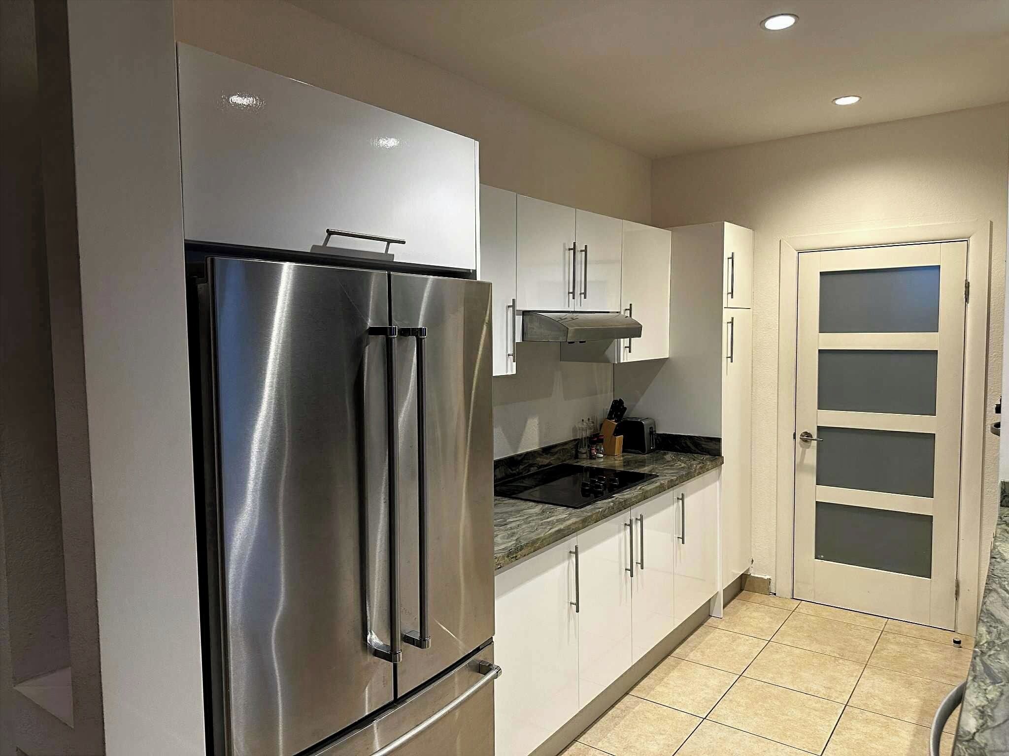 Una cocina moderna con electrodomésticos de acero inoxidable, armarios blancos y piso de baldosas.