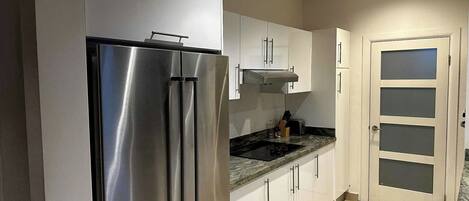 Una cocina moderna con electrodomésticos de acero inoxidable, armarios blancos y piso de baldosas.