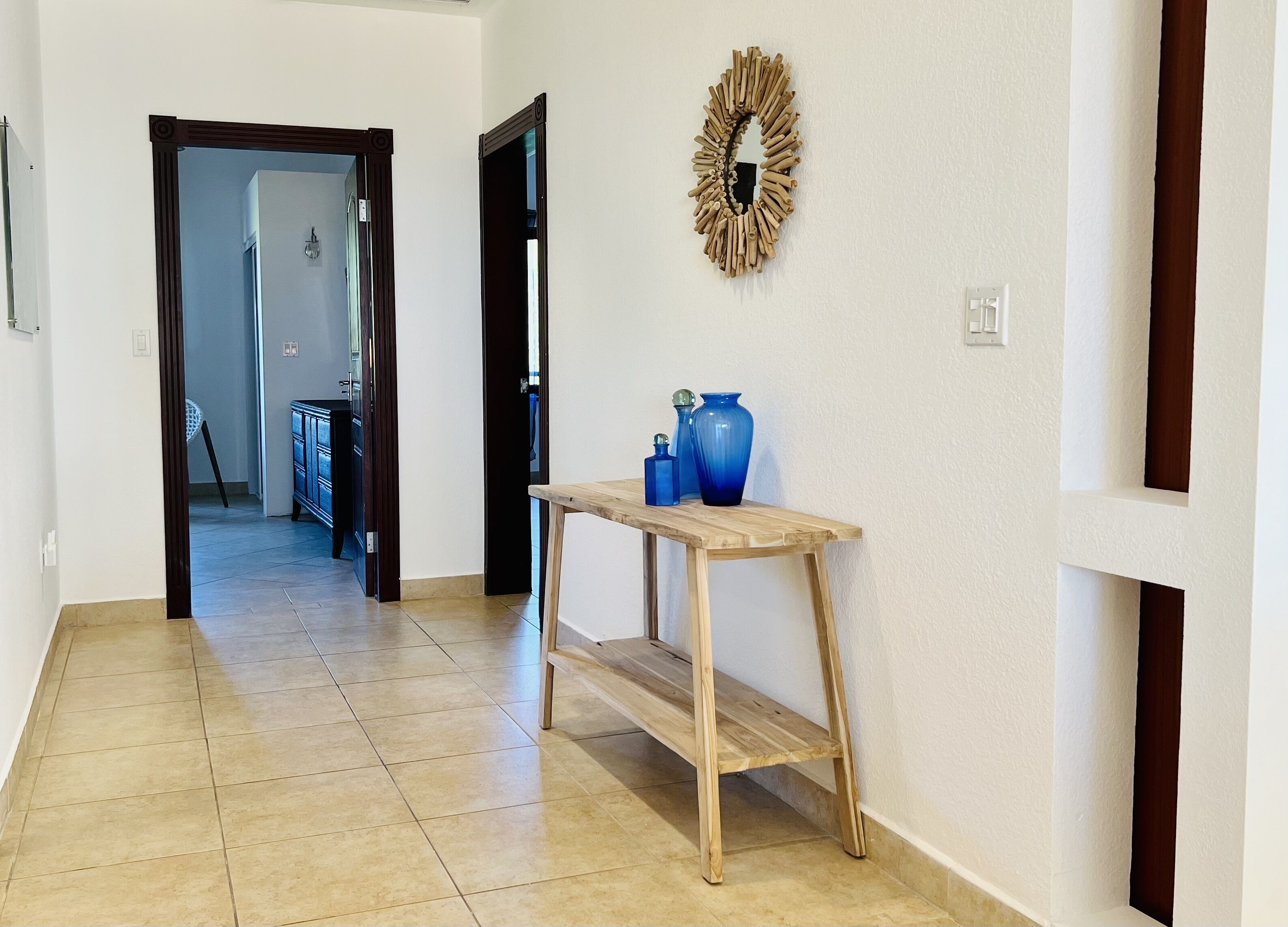 Een gang met een houten console tafel, een blauwe vaas en een decoratieve krans aan de muur.