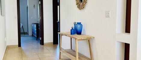 Een gang met een houten console tafel, een blauwe vaas en een decoratieve krans aan de muur.