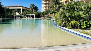 A swimming pool with a clear blue water, surrounded by palm trees and a building with multiple balconies. - Rendez-vous in St-Martin - Tropical Waves (Sint Maarten)