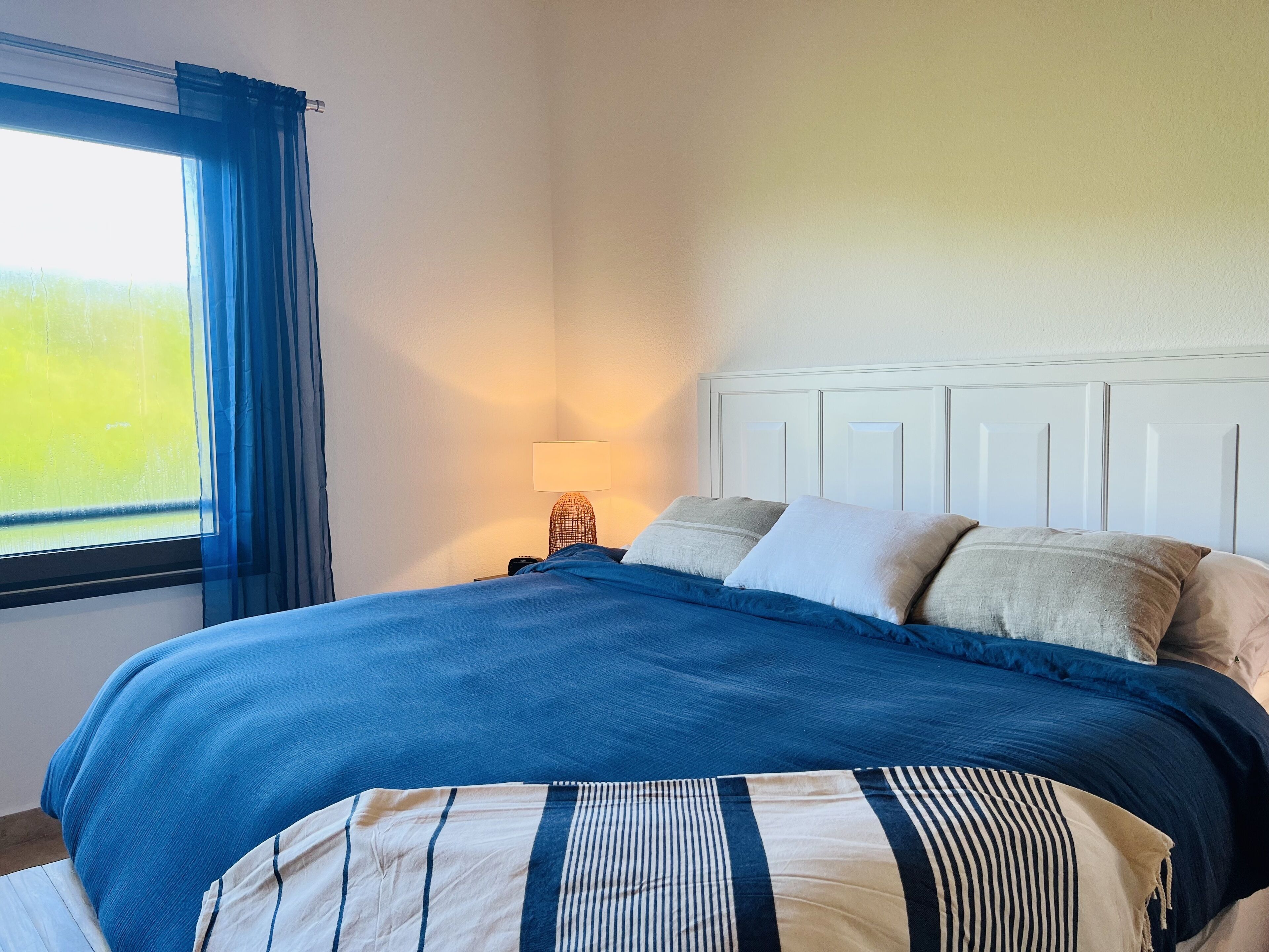 A neatly made bed with a blue and white striped bedspread, a white headboard, and a bedside lamp.
