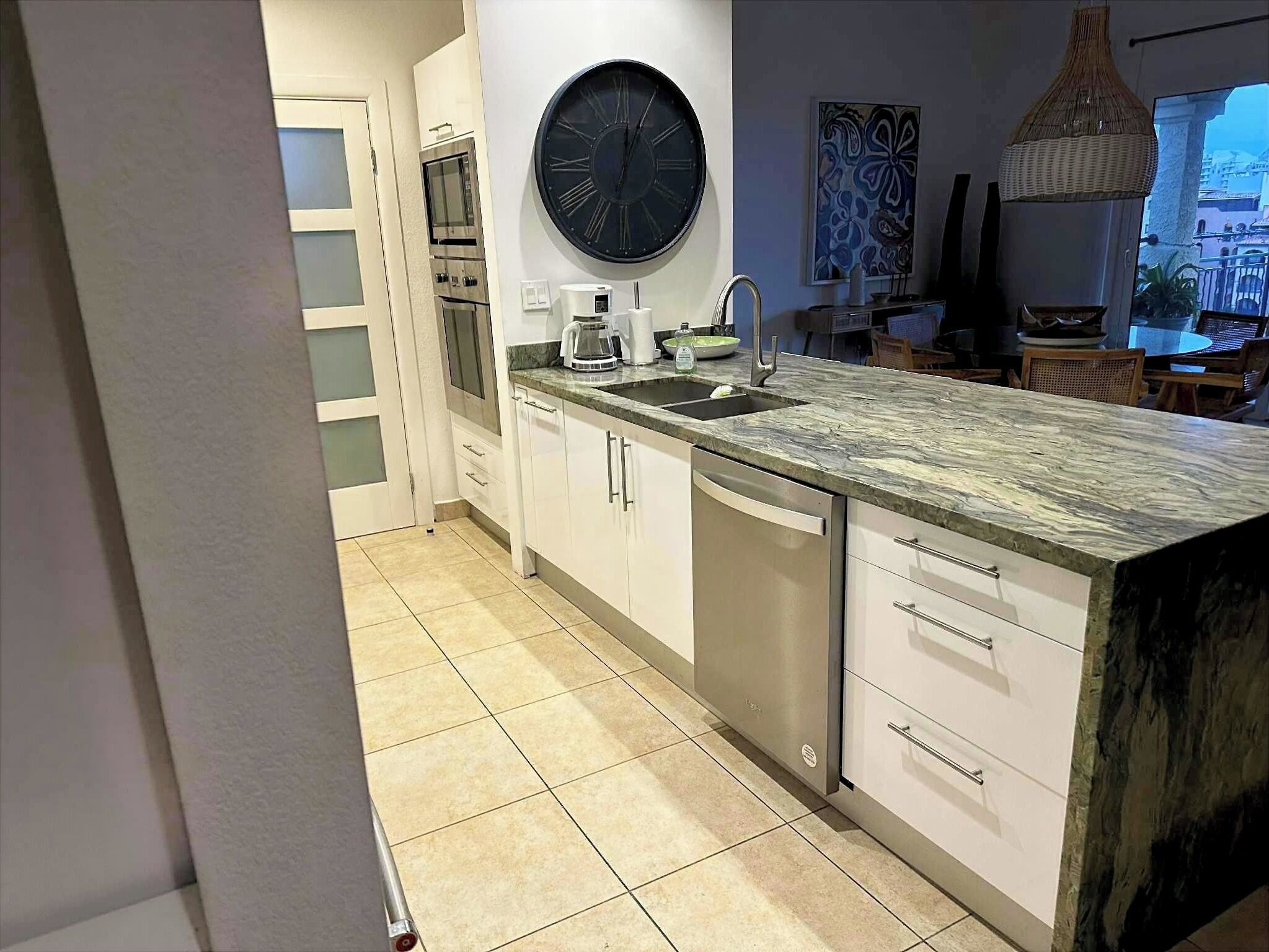 A modern kitchen with a large island, built-in oven, and a round wall clock.
