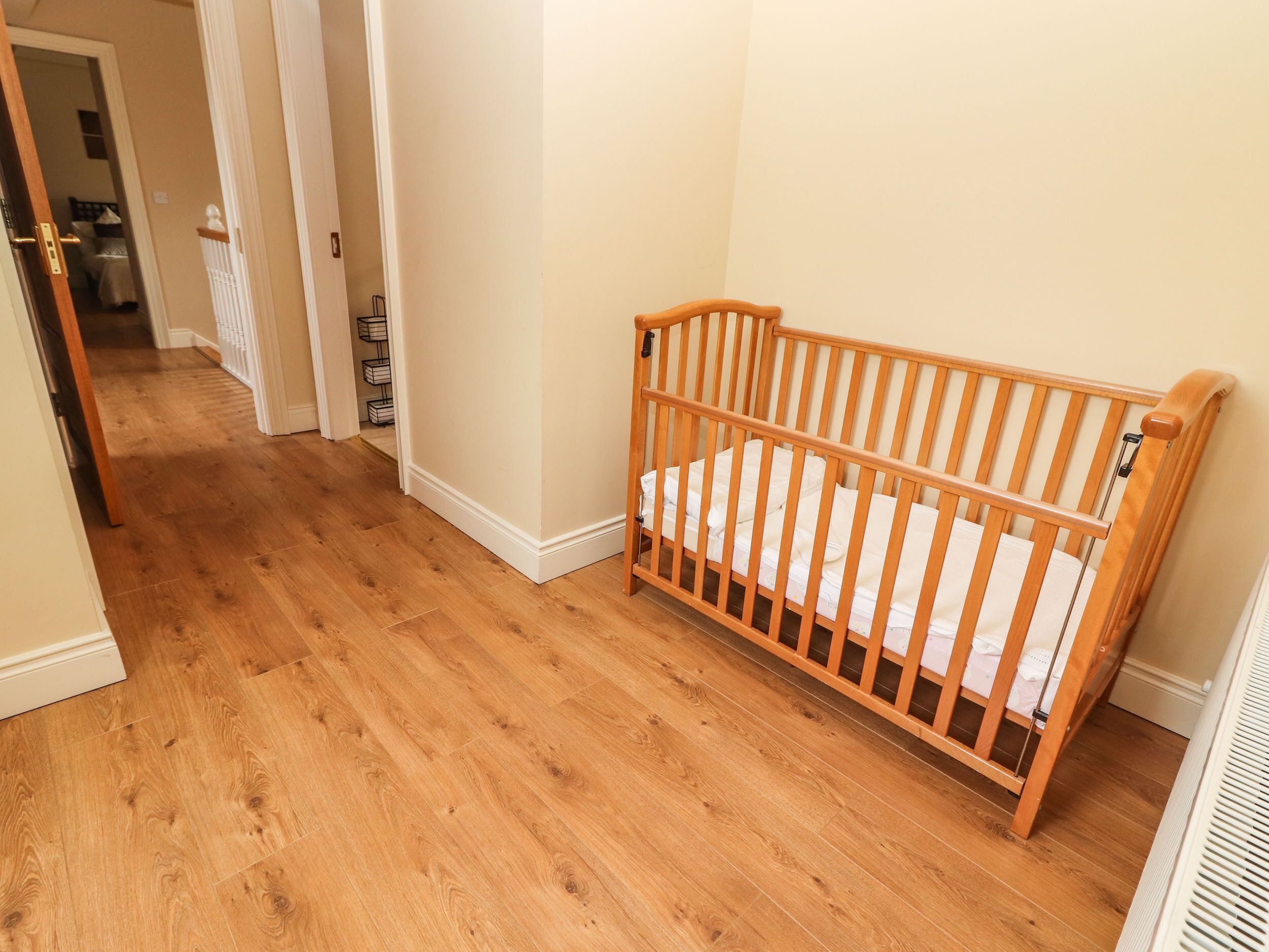 A wooden crib in a hallway with wooden flooring and white walls.