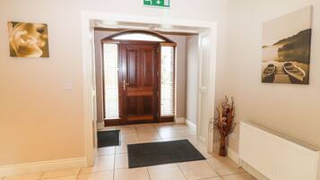 A hotel entrance with a wooden door, a green emergency exit sign, a doormat, a radiator, and two paintings on the walls.