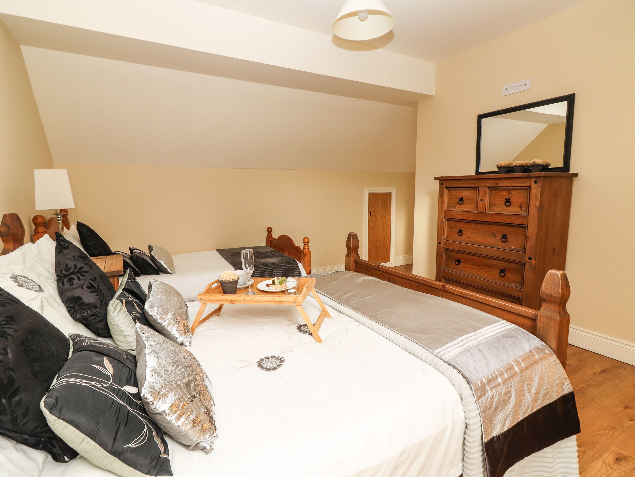 A bedroom with two beds, a wooden dresser, a mirror, and a bedside table with a lamp.