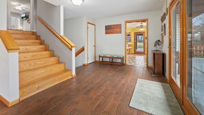 A spacious living area with a wooden staircase, a bench, and a view through a glass door. - Ninnie & Papaw's Paradise Cove on Beaver Lake (Springdale)