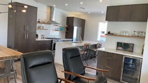 Una cocina moderna con armarios oscuros, una isla central y una zona de comedor con dos sillas negras.