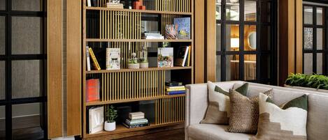 Una sala de estar moderna con una estantería de madera, un sofá color beige con cojines decorativos y una mesa de centro con libros.
