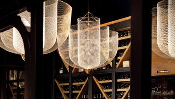 A restaurant with a long table set for dining, a wine rack in the background, and hanging woven light fixtures.
