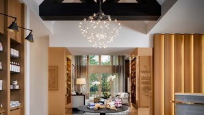 Un moderno vestíbulo de hotel con candelabro, estanterías de madera, un mostrador de recepción y vistas al exterior.