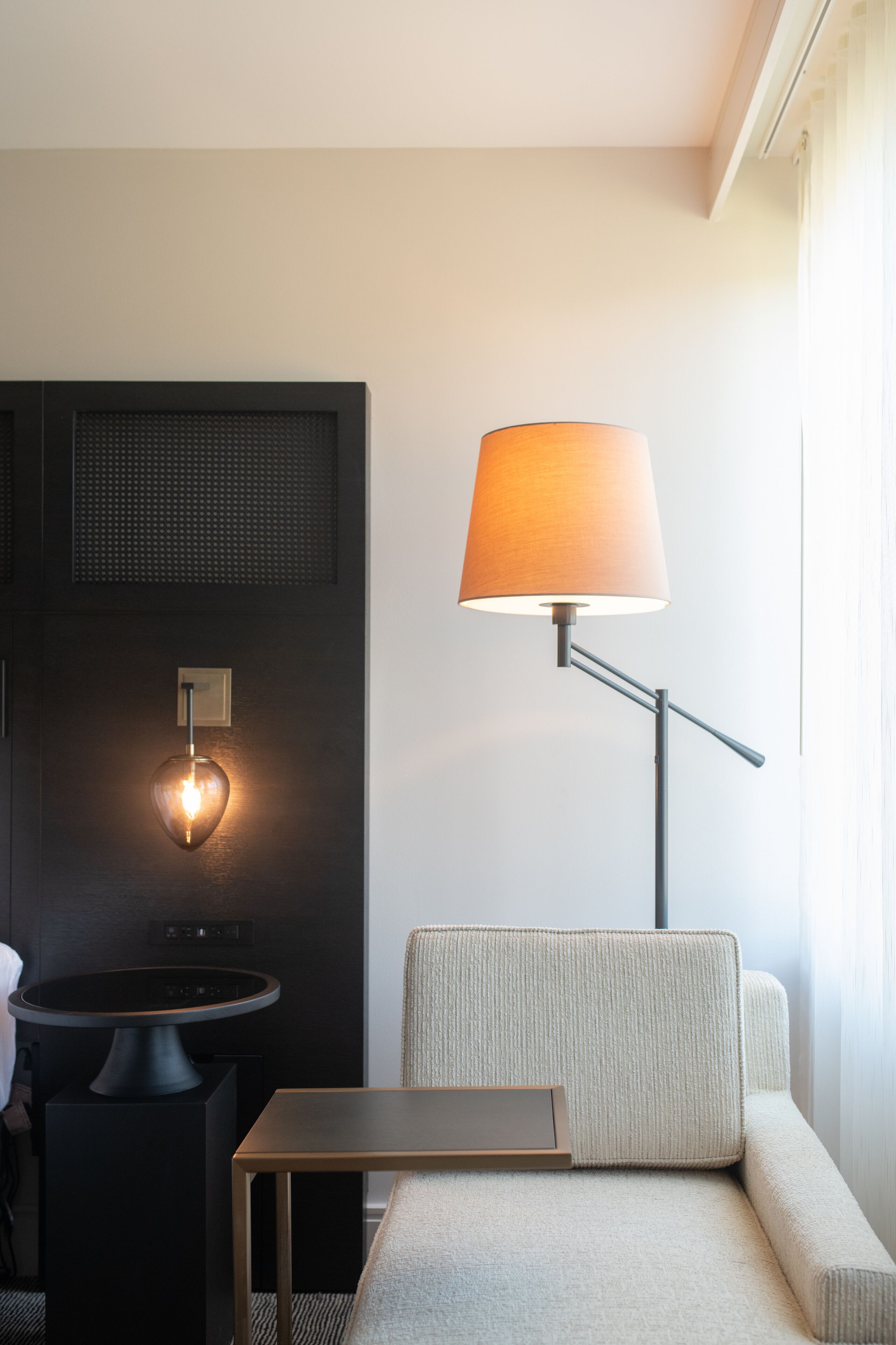 Ett modernt hotellrum med en soffa, ett litet bord, en lampa och en väggmonterad lamparmatur.