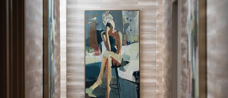A hallway with a framed painting of a woman sitting by a pool.
