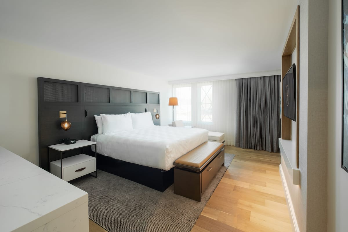 A modern hotel room with a large bed, bedside tables, a bench, and a flat-screen TV.