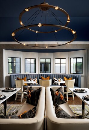 A modern interior with a circular chandelier, seating arrangements, and large windows. - Hotel Hartness (Greenville)