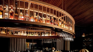 Un bar con varias estanterías llenas de botellas de licores y copas colgadas.