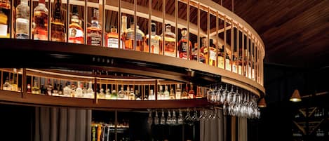 A bar with multiple shelves of liquor bottles and glasses hanging above.
