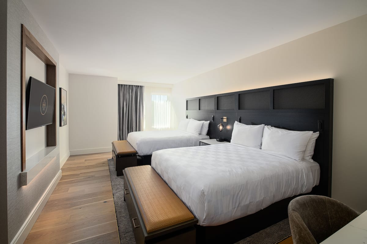 A hotel room with two beds, a bench, a desk, and a TV.
