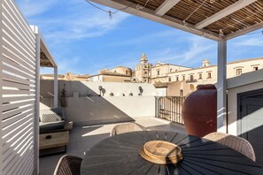 A terrace with a table, chairs, and a view of historic buildings. - Donna Rosa Holiday Home - Terrazza (Noto)
