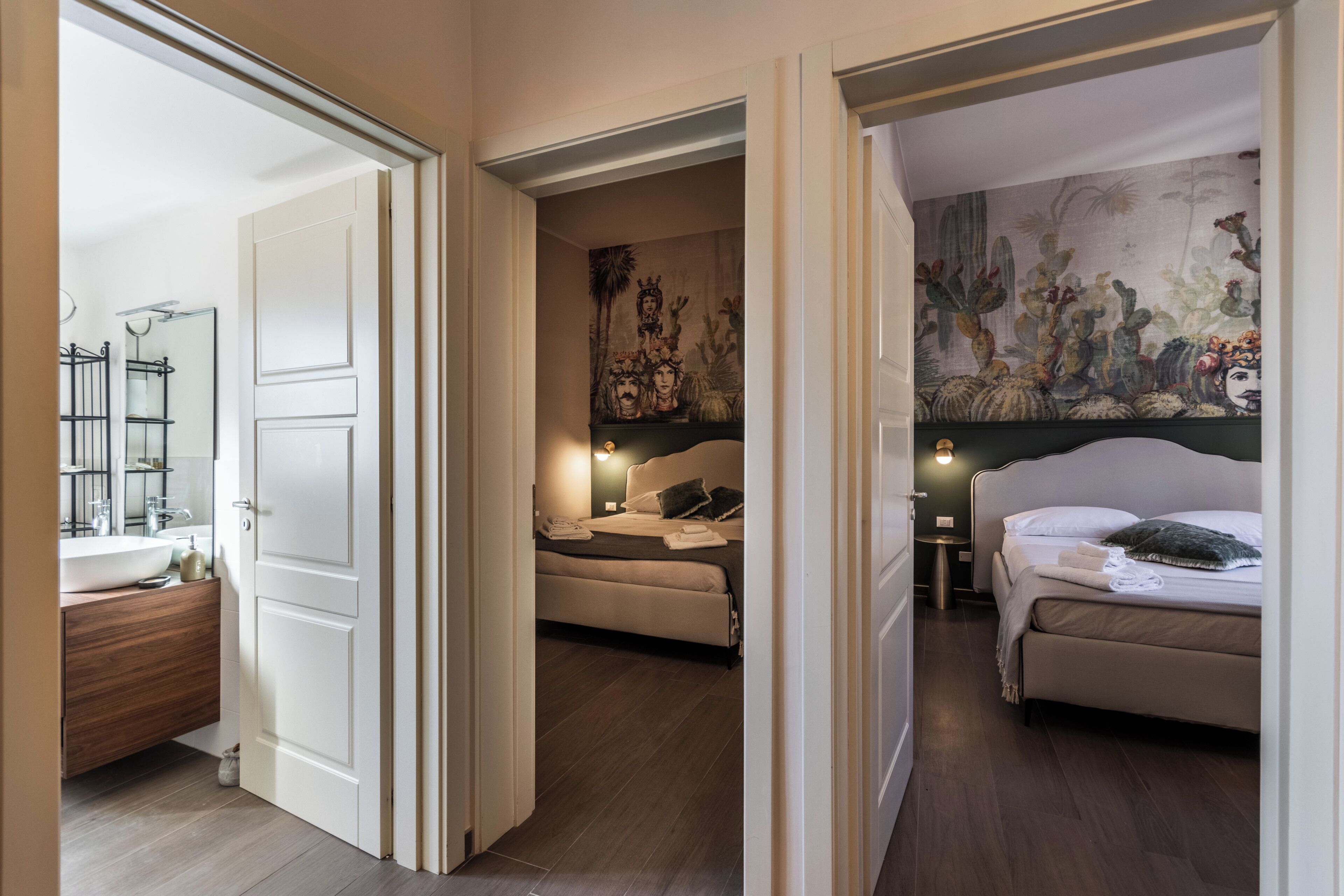A hotel room with a bathroom, a bed, a nightstand, and a wall with a cactus mural.