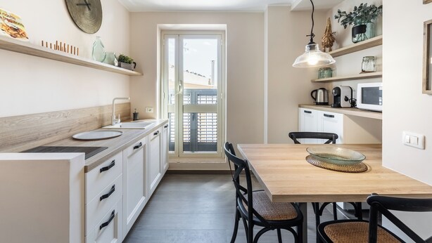 A modern kitchen with white cabinetry, a wooden countertop, a dining table with chairs, and a large window. - Donna Rosa Holiday Home - Vicolo (Noto)