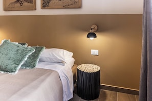 A bedroom with a bed, pillows, a wall-mounted lamp, and a round wooden stool.