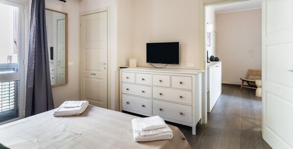 A hotel room with a bed, a dresser, a television, and a view of the hallway.