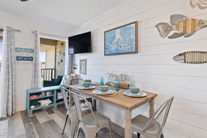 Un coin repas avec une table en bois dressée pour quatre personnes, entourée de chaises. Un téléviseur est fixé au mur au-dessus de la table.