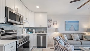 A modern kitchen with stainless steel appliances, a dining area with a patterned sofa, and a ceiling fan.