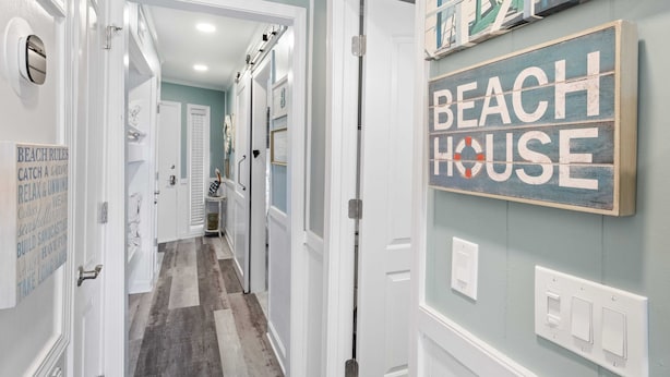 A hallway with a sign reading "BEACH HOUSE" on the wall, white doors, and a wooden floor.