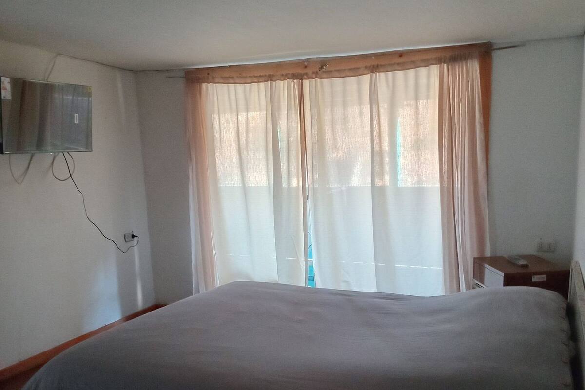 Ein Schlafzimmer mit einem großen Bett, einem an der Wand befestigten Fernseher und einem Fenster mit Vorhängen.