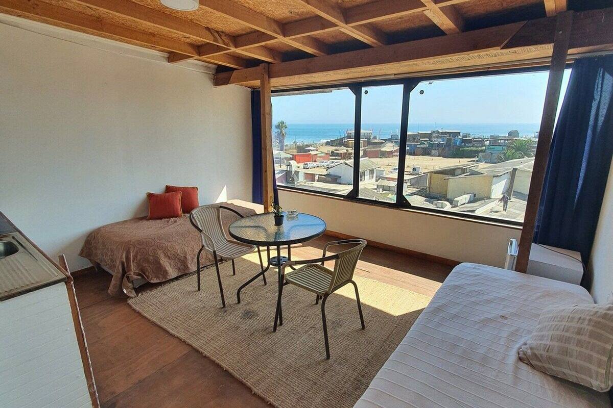 Ein Zimmer mit einem Bett, einem kleinen Tisch mit Stühlen, einer Couch und Blick auf Stadt und Meer durch große Fenster.