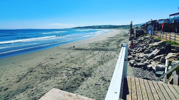 Una playa con un paseo marítimo de madera que lleva a un edificio con ventanas grandes.