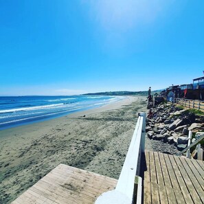 A beach with a wooden boardwalk leading to a building with large windows. - Bocamar Apart Hotel  (Concon)