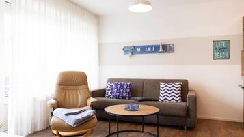 Un salon avec un fauteuil en cuir marron, un canapé gris orné de coussins à motifs, une table basse ronde et un panneau mural sur lequel on peut lire « MOLÉI ».