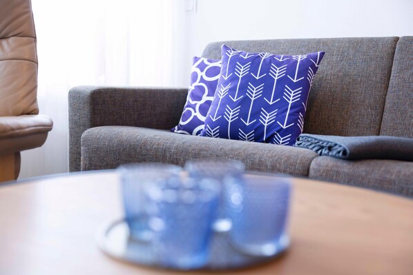 Un sofá gris con un cojín estampado, un control remoto y una mesa de centro con una taza azul.