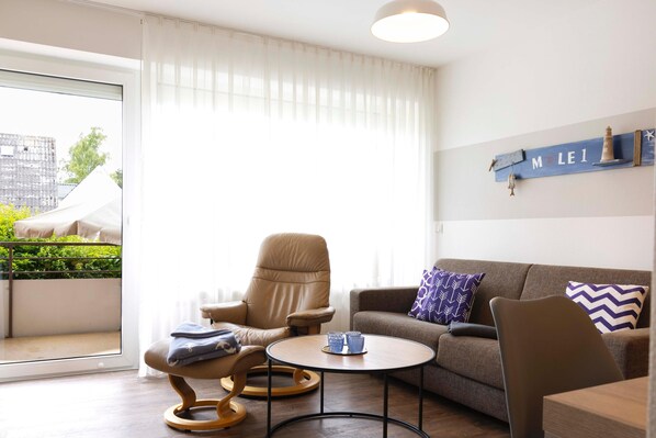 A modern living room with a sofa, two armchairs, a coffee table, and a balcony with a view of greenery and a building. - Vacation apartment "Mole 1" up to 4 persons (non-smoking) (Niendorf/Ostsee)