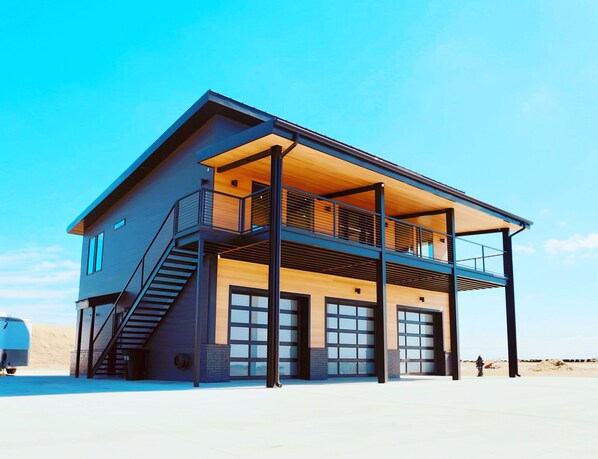 Une maison moderne à deux étages, dotée d’un balcon, de grandes fenêtres et d’un garage.