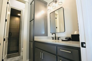 Une salle de bain moderne avec une douche à l’italienne, un grand miroir et un meuble-lavabo doté d’un nécessaire de maquillage.